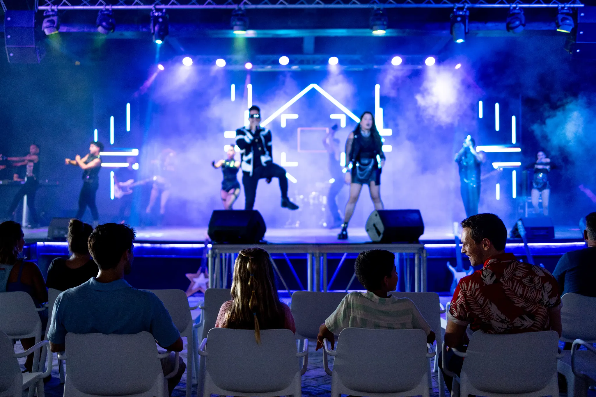 Family watching a live stage performance with lights and dancers at Sunscape Dominicus La Romana.