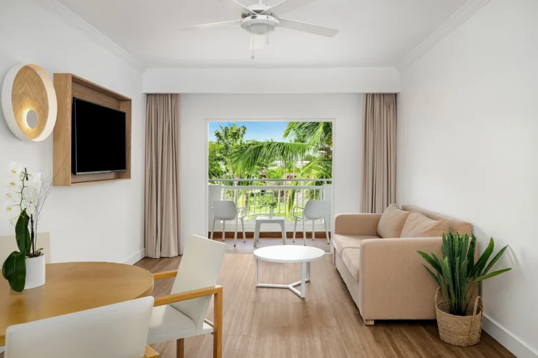 Sun Club Master Suite Two Bedroom Ocean View living area with sofa, dining table, and balcony overlooking tropical greenery at Sunscape Dominicus La Romana.